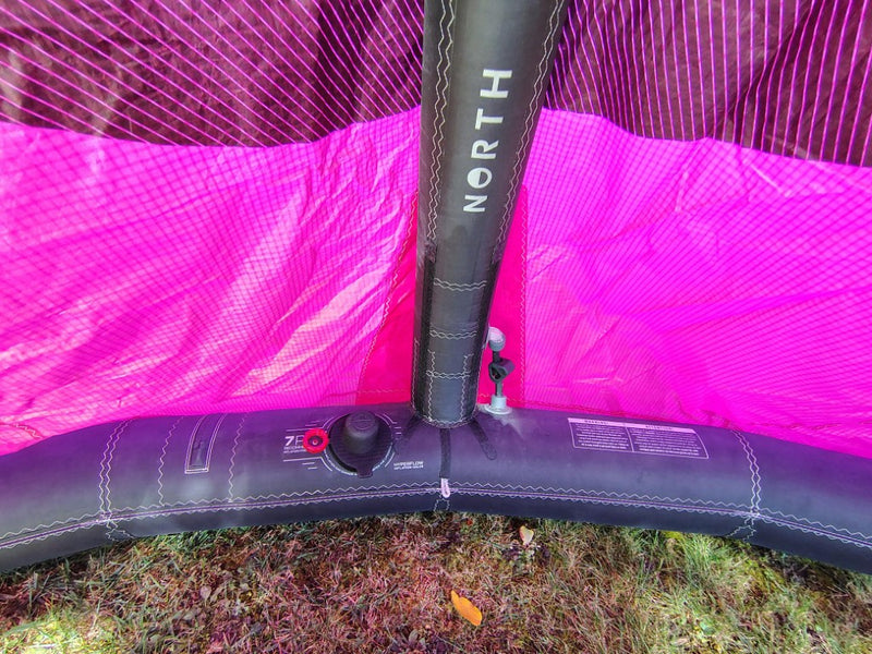 Load image into Gallery viewer, Green Hat Kiteboarding-2024 12m North Reach Kite-Close Up View of Valve and Center Strut-Pink kite with 'North' branding on a grassy area
