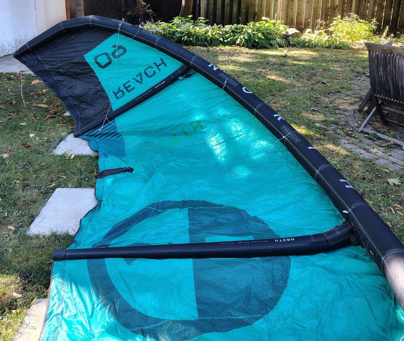 Load image into Gallery viewer, Green Hat Kiteboarding-2024 9m North Reach Kite-Inside Left Wing Tip View of Turquoise kite with 'North' branding on a grassy area