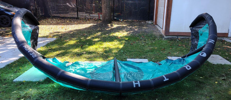 Load image into Gallery viewer, Green Hat Kiteboarding-2024 9m North Reach Kite-Upside Down Leading Edge View of Turquoise kite with 'North' branding on a grassy area
