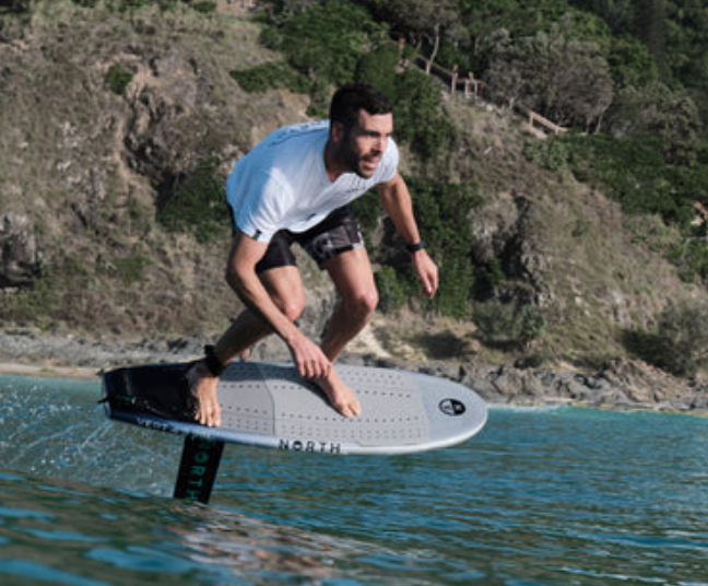 Load image into Gallery viewer, North Vert Prone Foil Board-Action Shot-Man Foil Surfing on a Wave with a Scenic Background