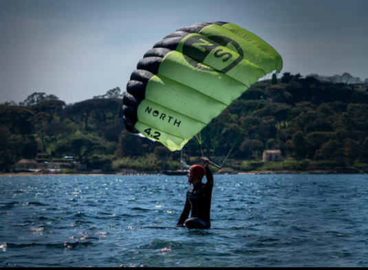 Green Hat Kiteboarding-North Ranger Parawing-Action Shot-Man Sitting on Board in the Water with Ranger Parawing in the Air