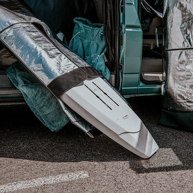 Load image into Gallery viewer, Green Hat Kiteboarding-Manera Prone Foilboard Bag-White foilboard with a black strap leaning against a vehicle on a road.