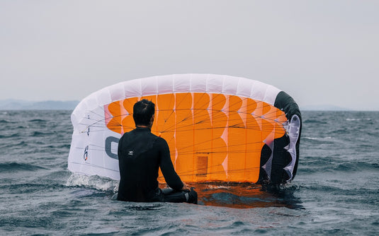 Green Hat Kiteboarding-Ozone Pocket Rocket Parawing-Man Sitting on a Foilboard Launching the Pocket Rocket