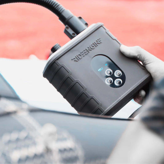 A person holding the Ride Engine Air Box Electric Pump, a rechargeable electric pump for kites, wings, and boards. It has a two-stage system for fast inflation and real-time pressure monitoring.