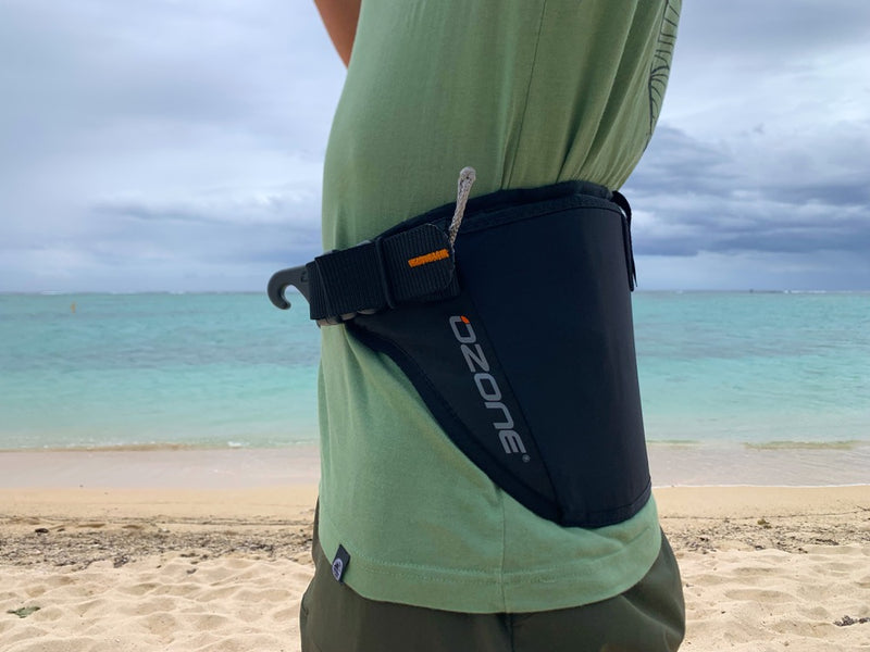 Load image into Gallery viewer, Person wearing a black Ozone Parawing Stash Harness on a beach with ocean in the background