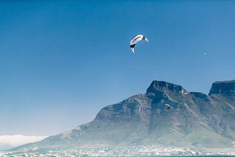 Load image into Gallery viewer, A person flying the Core XR7 Kiteboarding Kite over a mountain, showcasing the thrill of kite sports in the sky.
