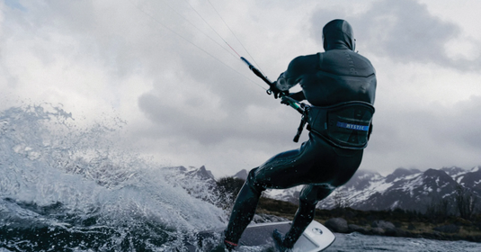 Green Hat Kiteboarding-Mystic Stealth Harness with rope slider-Kiter riding on a lake surrounded by mountains-snow on the peaks