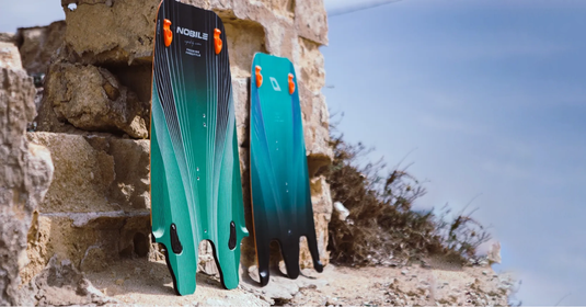 Kiteboarding Splitboards: Slash Luggage Expenses-Nobile NHP Carbon Split Kite Board-Board split in half leaning against a rock wall-Board is Black and Green-Green Hat Kiteboarding