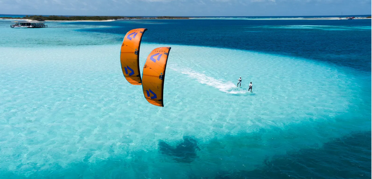 Green Hat Kiteboarding-Duotone Rebel SLS-Inflatable Kite-Red and navy-2 kiters riding on a clear blue ocean 