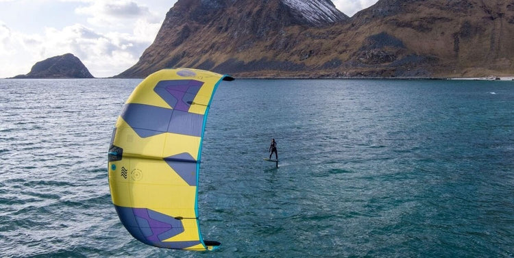 Green Hat Kiteboarding-Kite Foiling Packages-Rider Kite Foiling a Duotone Dice Kite and a Duotone Pace Board in Front of Green Mountains