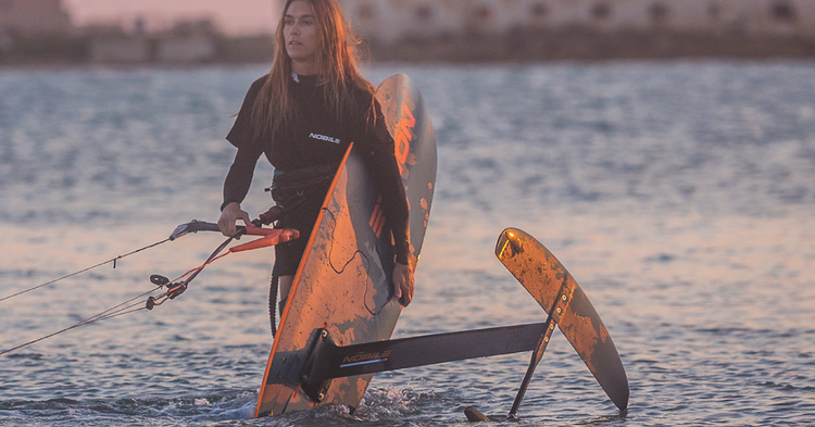 Green Hat Kiteboarding-Nobile-Woman holding Nobile Kite Foil Split Board in shin deep water-