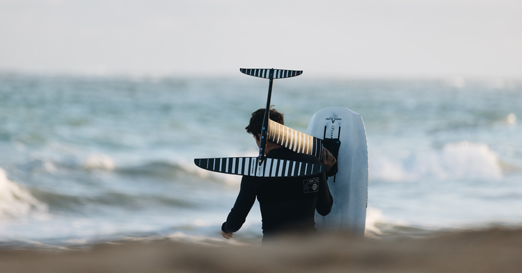 Green Hat Kiteboarding-Wing Foil Component Collection Image-Winger walking toward the Ocean with His Armstrong Foil on his Shoulder