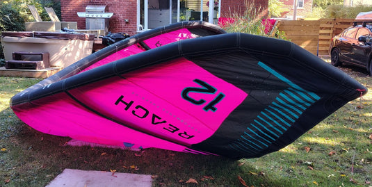 Green Hat Kiteboarding-2024 12m North Reach Kite- Up Side Down Left Wing Tip View-Pink kite with 'North' branding on a grassy area