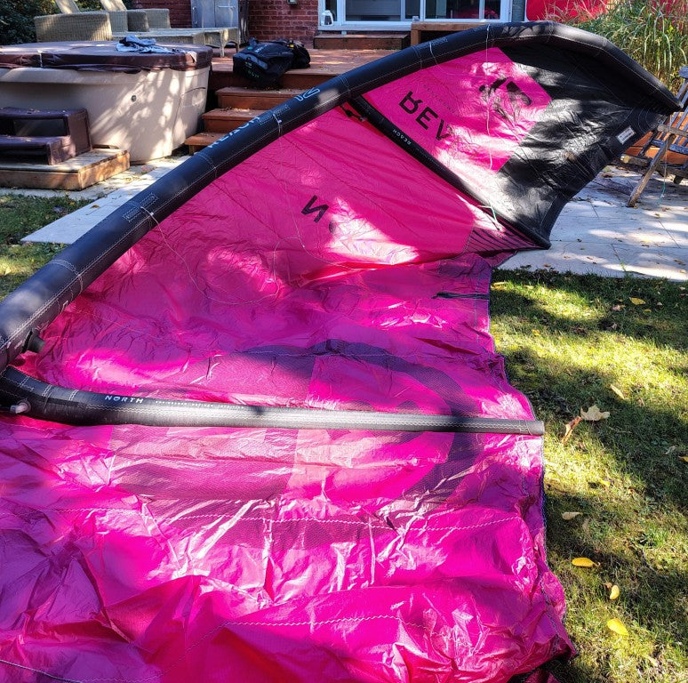 Load image into Gallery viewer, Green Hat Kiteboarding-2024 12m North Reach Kite- Inside Right Wing Tip View-Pink kite with &#39;North&#39; branding on a grassy area 

