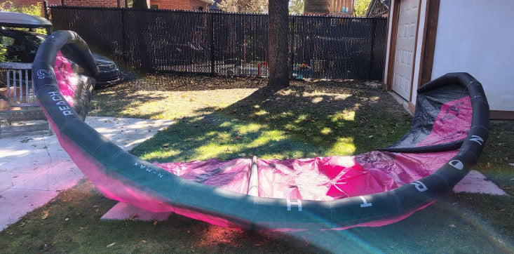 Load image into Gallery viewer, Green Hat Kiteboarding-2024 12m North Reach Kite- Up Side Down Leading Edge View-Pink kite with &#39;North&#39; branding on a grassy area with Bag
