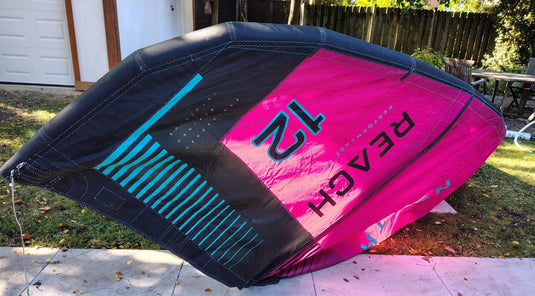 Green Hat Kiteboarding-2024 12m North Reach Kite-Upside Down Right Wing Tip View-Pink kite with 'North' branding on a grassy area 