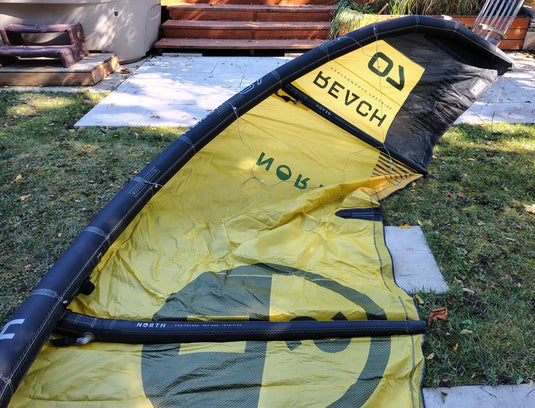 Green Hat Kiteboarding-2024 7m North Reach Kite-Inside Right Wing Tip View of Sunset Yellow kite with 'North' branding on a grassy area 