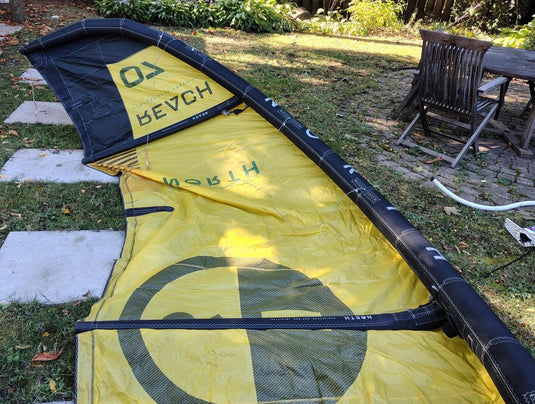 Green Hat Kiteboarding-2024 7m North Reach Kite-Inside Left Wing Tip View of Sunset Yellow kite with 'North' branding on a grassy area 