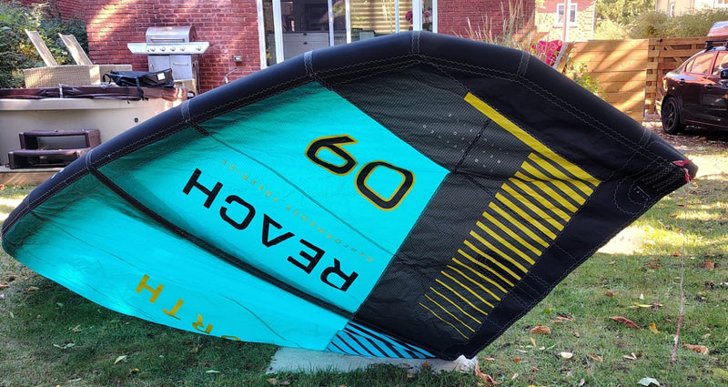 Load image into Gallery viewer, Green Hat Kiteboarding-2024 9m North Reach Kite-Left Upside Down Wing Tip View of Turquoise kite with &#39;North&#39; branding on a grassy area 
