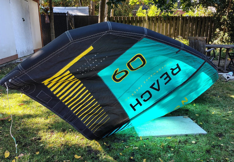 Load image into Gallery viewer, Green Hat Kiteboarding-2024 9m North Reach Kite-Right Upside Down Wing Tip View of Turquoise kite with &#39;North&#39; branding on a grassy area 
