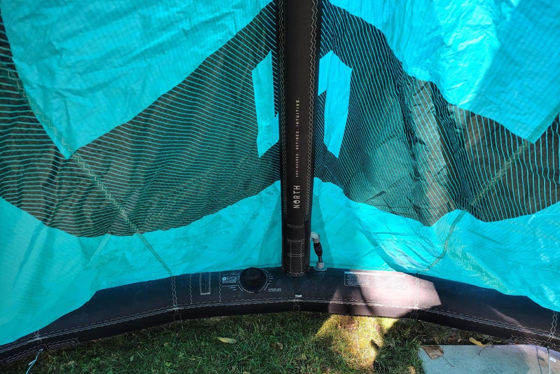 Load image into Gallery viewer, Green Hat Kiteboarding-2024 9m North Reach Kite-Close Up View of Valve &amp; Center Strut View of Turquoise kite with &#39;North&#39; branding on a grassy area
