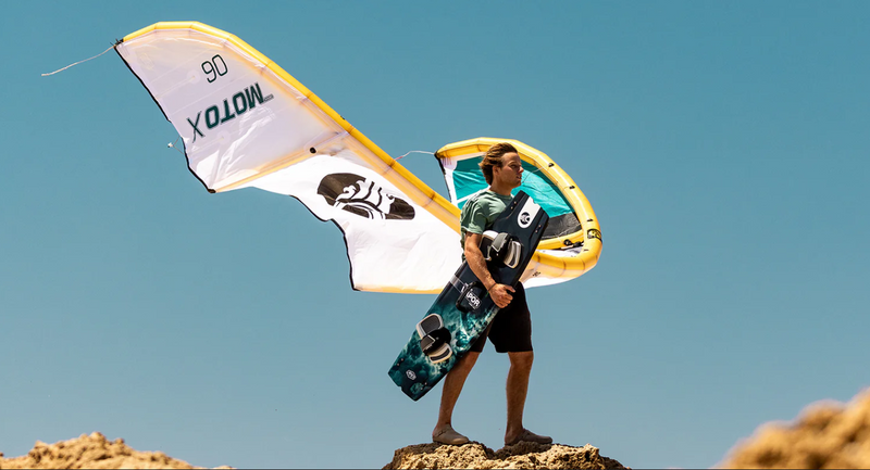 Load image into Gallery viewer, Green Hat Kiteboarding- 2024 Cabrinha Moto X Design Works Kite-Live Shot-Man on a Cliff Holding a Cabrinha Moto X Design Works Kite
