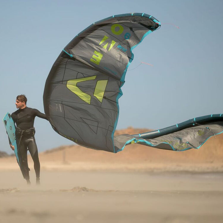 Green Hat Kiteboarding-Duotone Evo D/LAB Limited Edition-Live Shot-Man on the Beach Holding a Duotone EVO D/LAB blue and a Duotone Kiteboard
