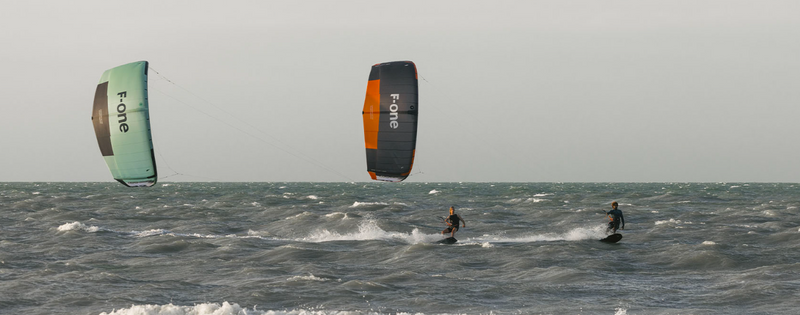 Load image into Gallery viewer, Green Hat Kiteboarding-2025_F-One_Bandit_TEC_Kite-Two Kiters Riding 2025 F-One Bandit TEC Kiteboard Kites of Different Colors
