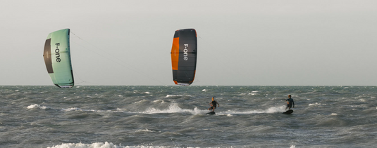 Green Hat Kiteboarding-2025_F-One_Bandit_TEC_Kite-Two Kiters Riding 2025 F-One Bandit TEC Kiteboard Kites of Different Colors