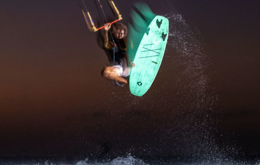 Green Hat Kiteboarding-2026 Duotone SLS Surfboard-Action Shot-Man Kiteboarding in the Air Riding a Whip SLS