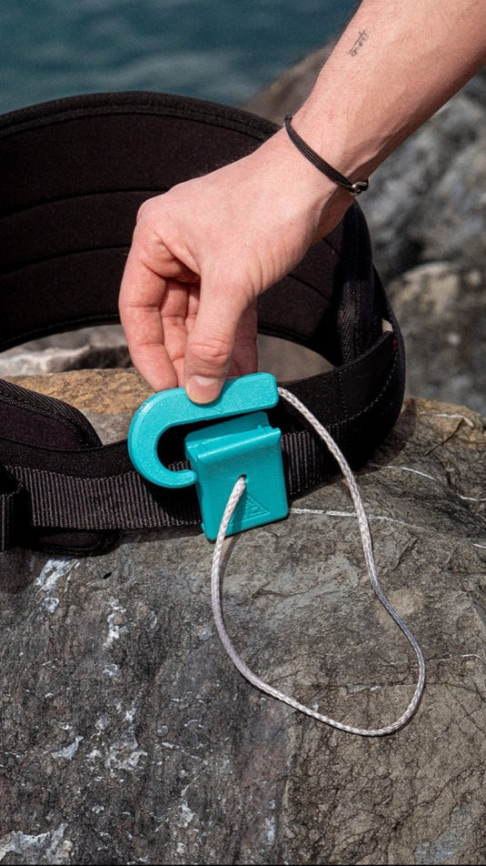 Person adjusting a A3D Magnetic Hook with a turquoise buckle on a rocky surface.