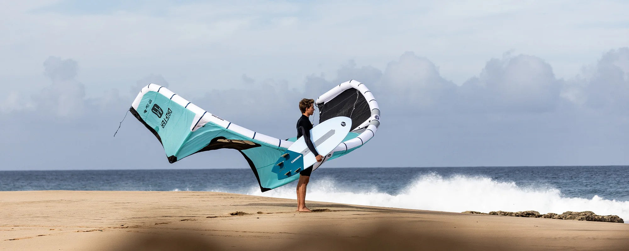 Green Hat Kiteboarding-Pages-All Packages-Kiteboarding Packages-Man Holding a Cabrinha Kite and Surfboard on the Beach
