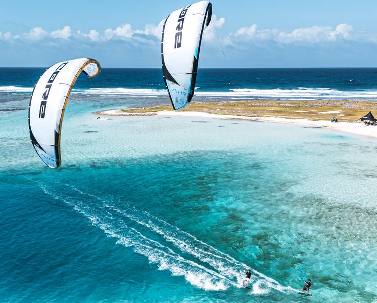 Green Hat Kiteboarding-Core AIR Kites-2 Kitesurfers in action with two large kites over a tropical beach and turquoise ocean.