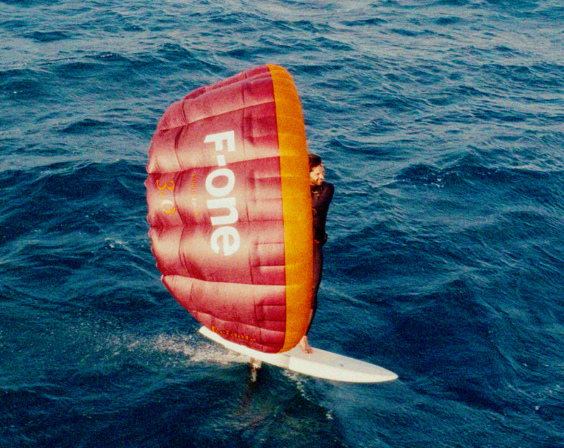 Load image into Gallery viewer, Green Hat Kiteboarding-F-One FRIGATE Parawing-Man parawinging with a pink and orange F-ONE parawing over blue ocean waters
