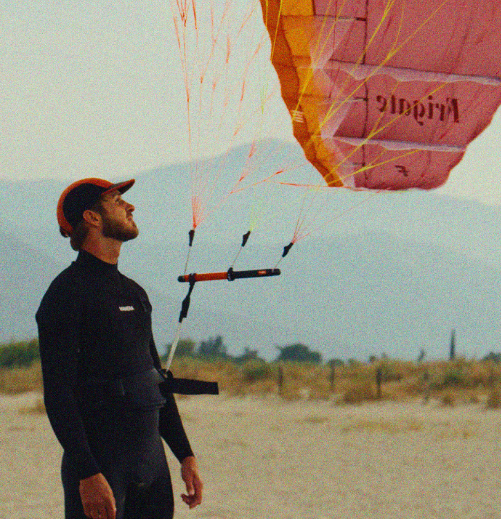 Load image into Gallery viewer, Green Hat Kiteboarding-F-One FRIGATE Parawing-Man holding with a harness line a pink &amp; orange parawing with mountains in the background
