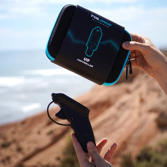 Person holding a black and blue controller box and a Foil Drive V3 Controller with 'Foil Drive' branding against a desert landscape.