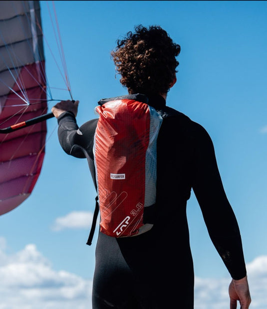 Person wearing a red  Flysurfer parawing backpack with a clear sky in the background