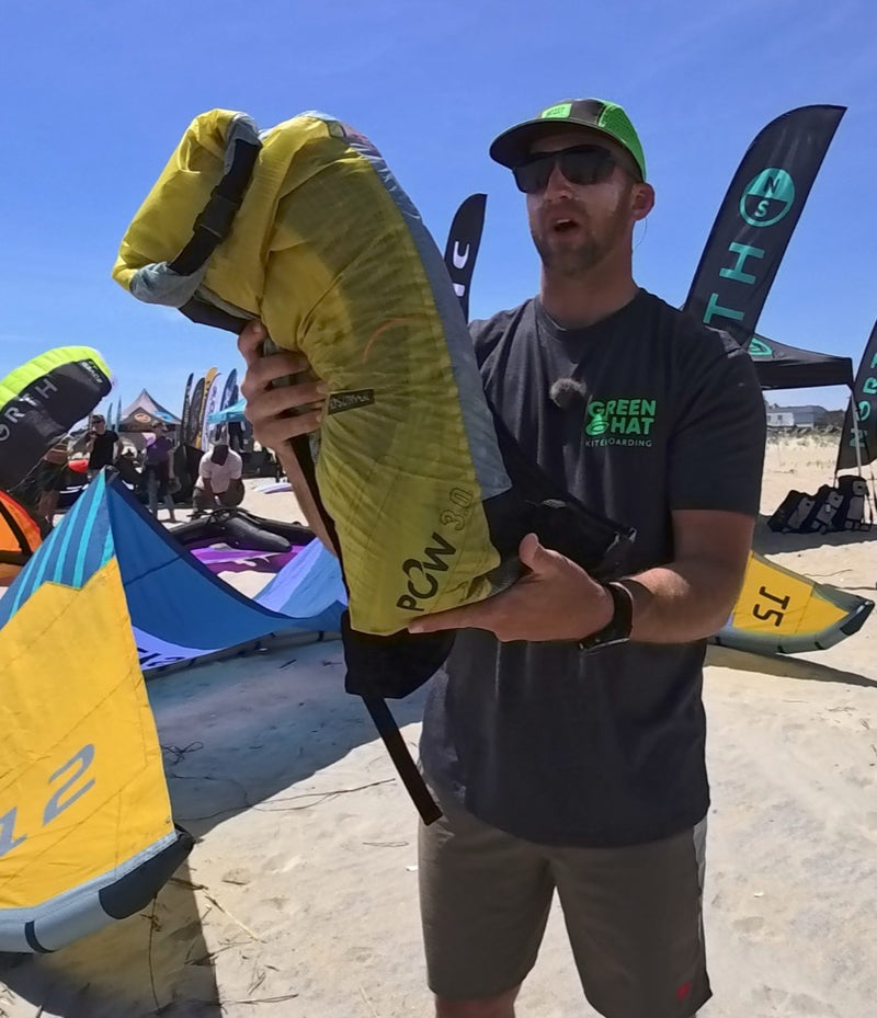 Load image into Gallery viewer, Man holding a Flysurfer POW2 Parawing Backpack on a beach with kites in the background.
