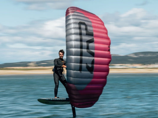 Person holding a Flysurfer ZAP Parawing over water with mountains in the background