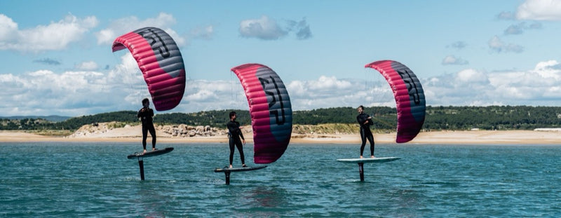 Load image into Gallery viewer, Three people parawinging in front of a beach with Flysurfer ZAP Parawings against a blue sky.
