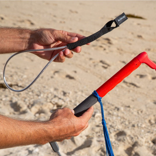 Green Hat Kiteboarding-Ozone Wing/Parawing Harness Line-Man holding a parawing bar in one hand and a harness line in the other against a sandy background