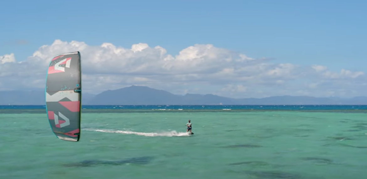 Green Hat Kiteboarding-Landing Page-All Packages-Man kiteboarding on clear blue water with a mountainous island in the background