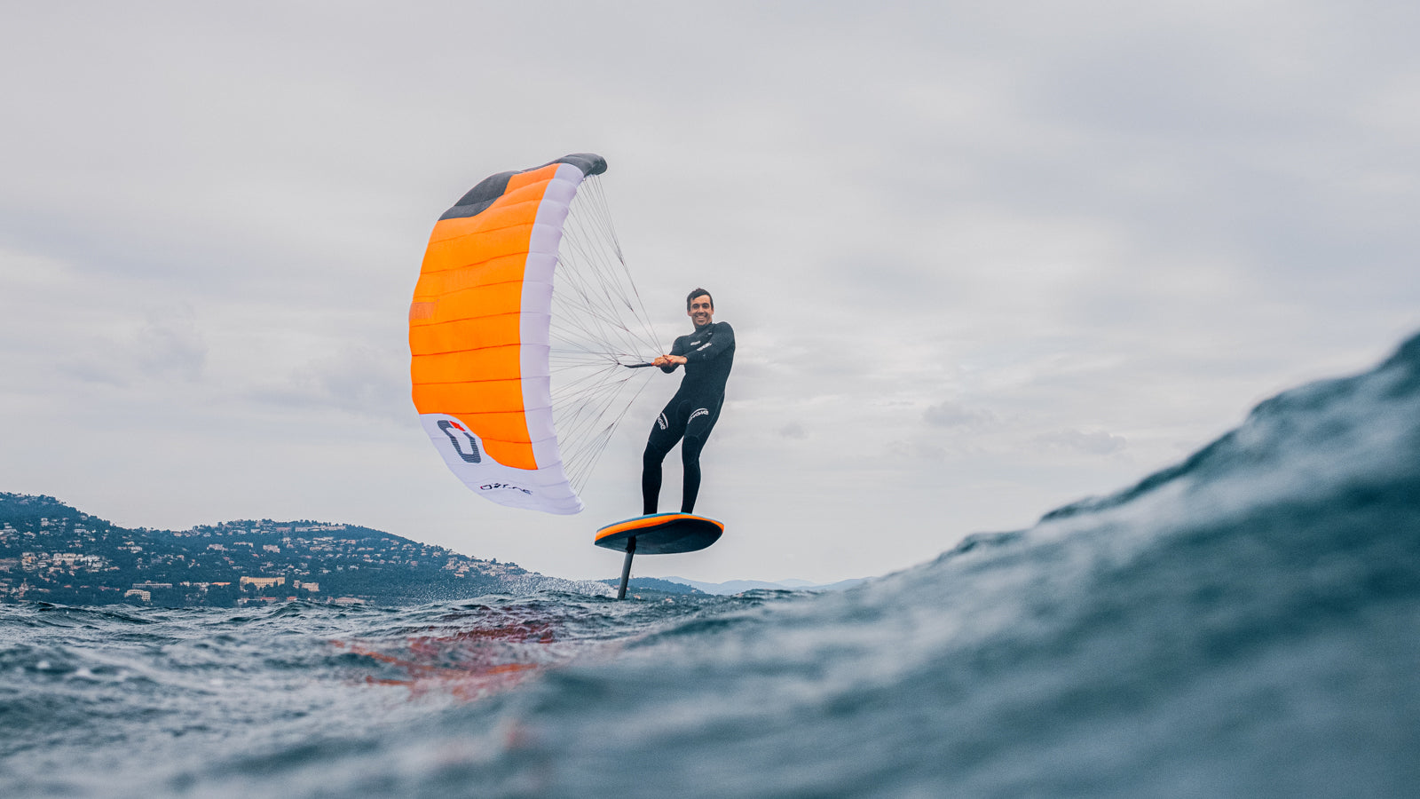 Green Hat Kiteboarding-Ozone Pocket Rocket Parawing-Man parawinging on a foilboard over a body of water.